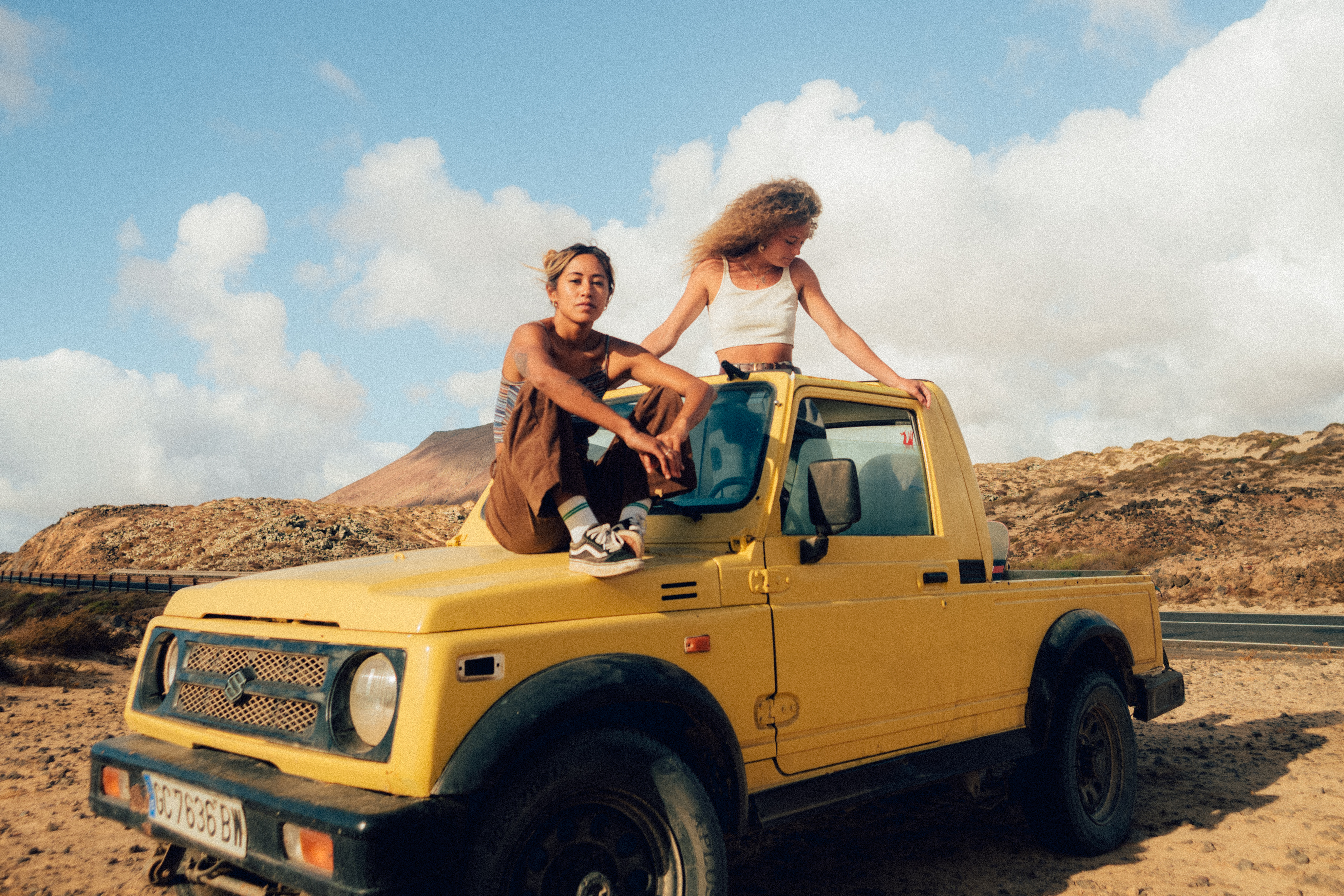 Two girl sitting on top of a yellow car